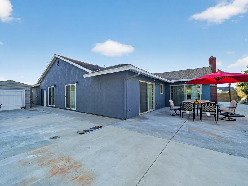 The back of the house with two patio dining sets and red umbrellas on a wide concrete patio