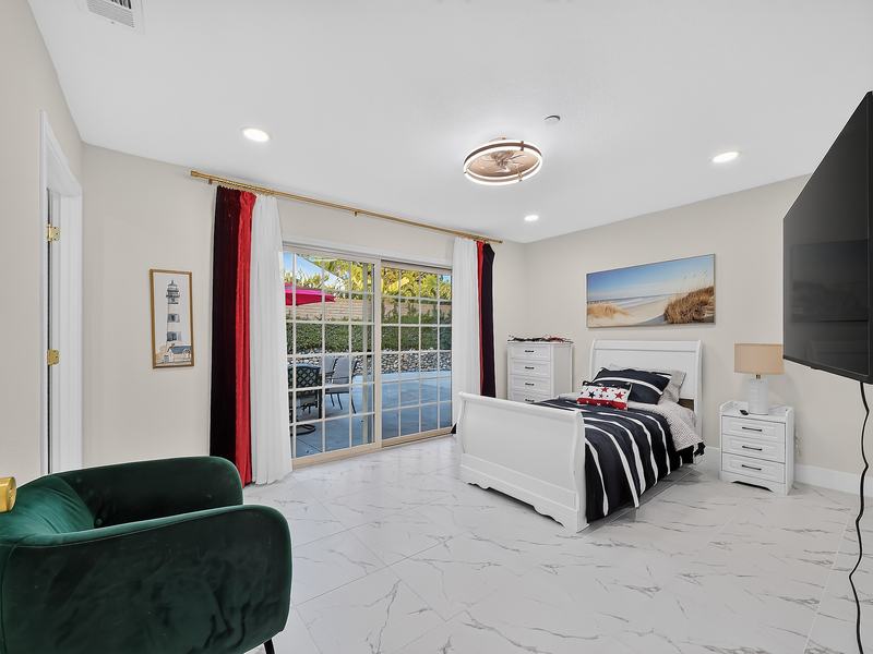 A bedroom with a sliding door to the patio, a green armchair, and a beach painting above the bed