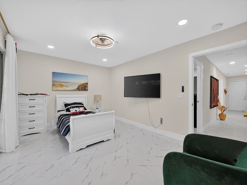 A bright bedroom with a white bed frame, a dresser, and a framed beach painting