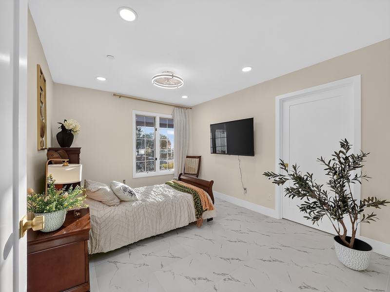 A calm bedroom in cream tones with a window onto the front garden and a potted olive tree
