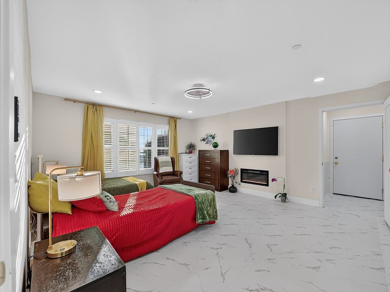 A large resident bedroom with a red bedspread, dresser, and its own electric fireplace