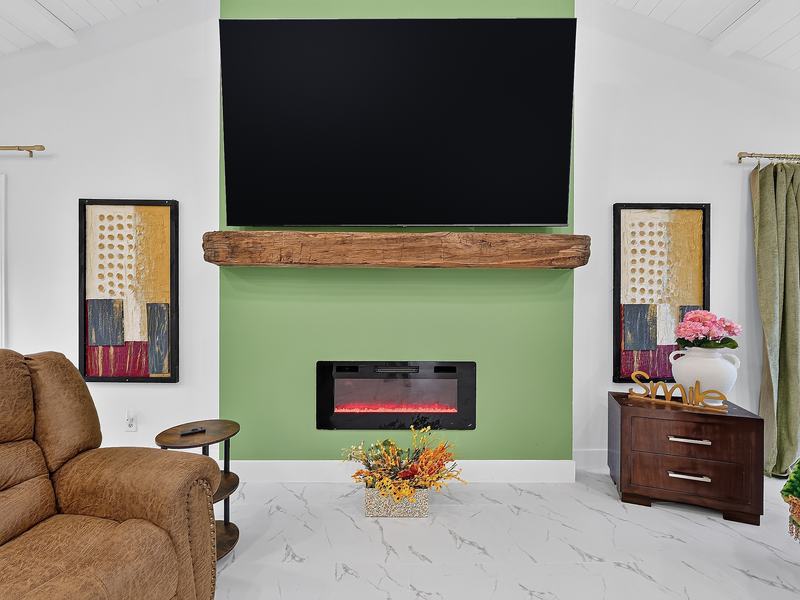 The fireplace wall in the great room: a green accent wall, rustic wood mantel, and lit electric fireplace