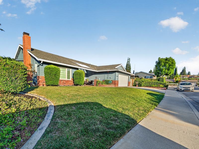 Front lawn and corner view of the house, with the brick chimney and neighborhood street