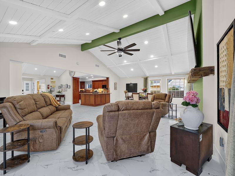 The great room seen from the dining table — recliners, the piano, and windows along two walls