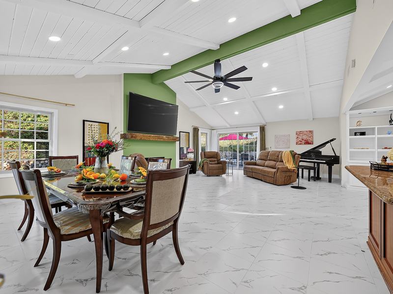 The open great room: dining table in front, sitting area and piano beyond, under a beamed vaulted ceiling