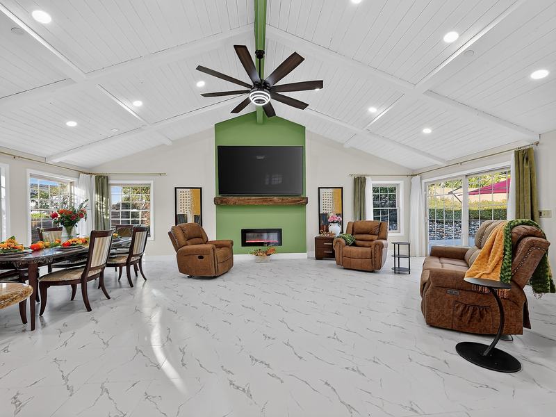 The living room with recliners and armchairs around the fireplace, lit by windows on two sides