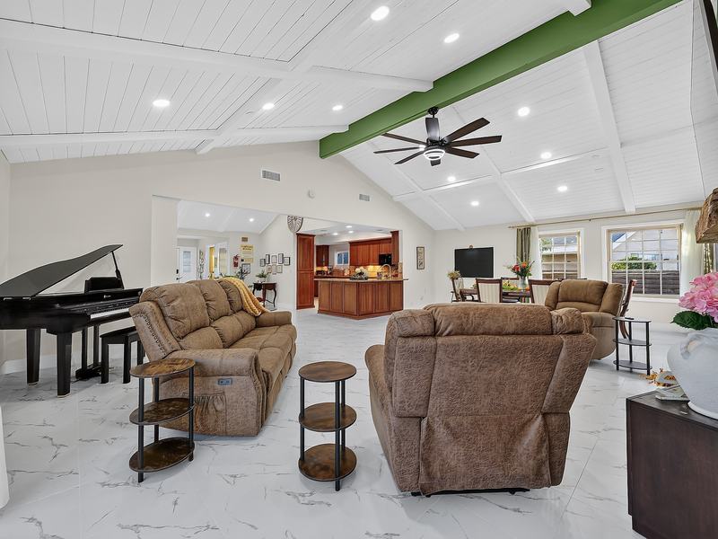 A sitting room with a grand piano, leather sofa, and glass doors to the backyard