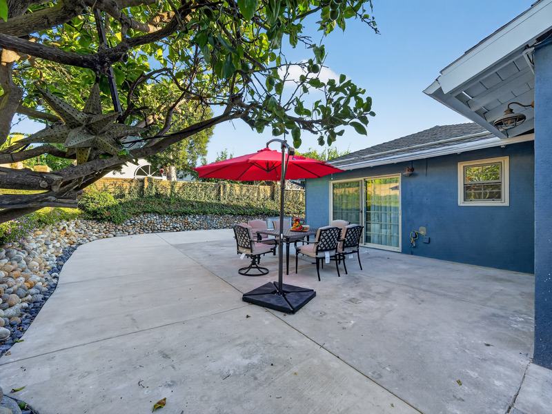 Backyard patio table and chairs under a red umbrella, shaded by a mature tree