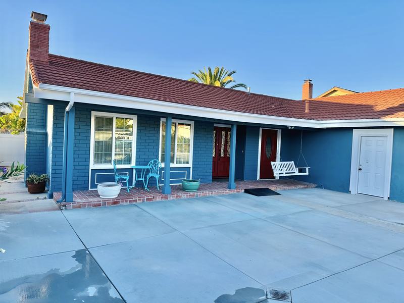 The front porch of Seniors Paradise — a blue single-story house with a red tile roof, red front doors, and a white porch swing